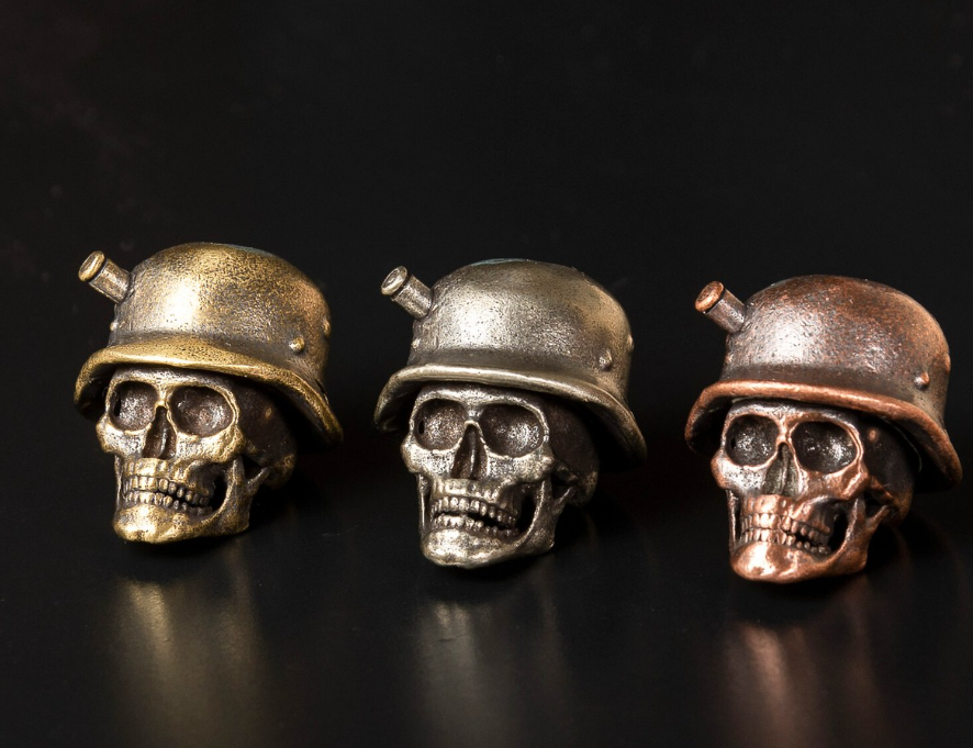 Brass, stainless steel, titanium, and polymer skull beads for paracord arranged side by side showing material differences