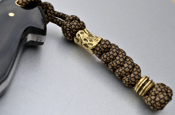 Close-up comparison of titanium, brass, and 316 stainless steel tactical paracord beads showing different finishes and weights