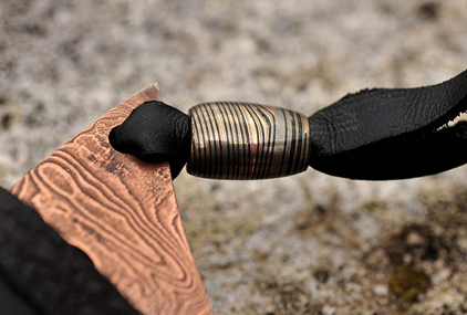 Hand applying oil to Damascus steel paracord bead with cloth demonstrating maintenance and corrosion prevention care